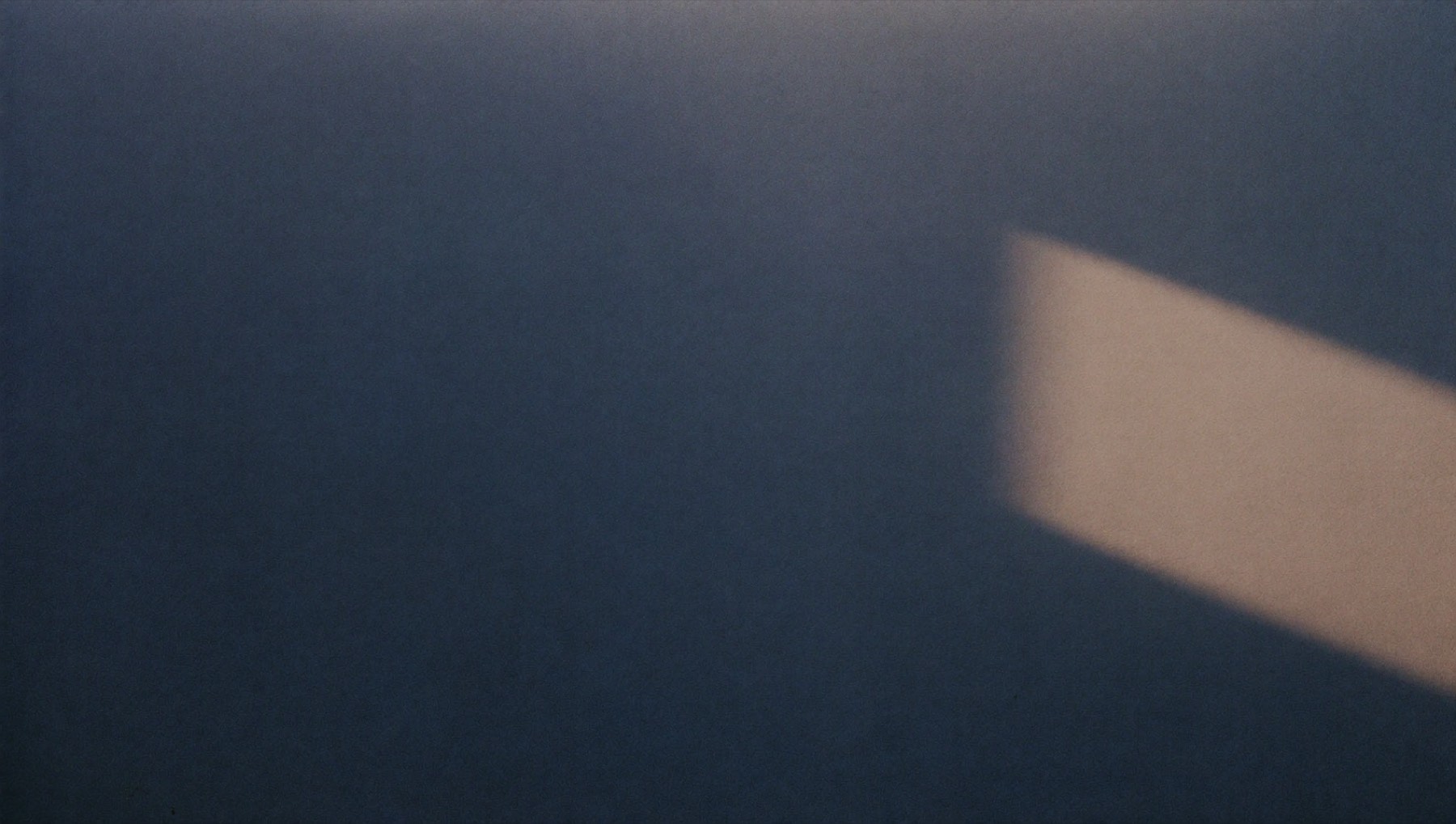 A single band of warm morning light on a deep blue wall, fading away at the edge.