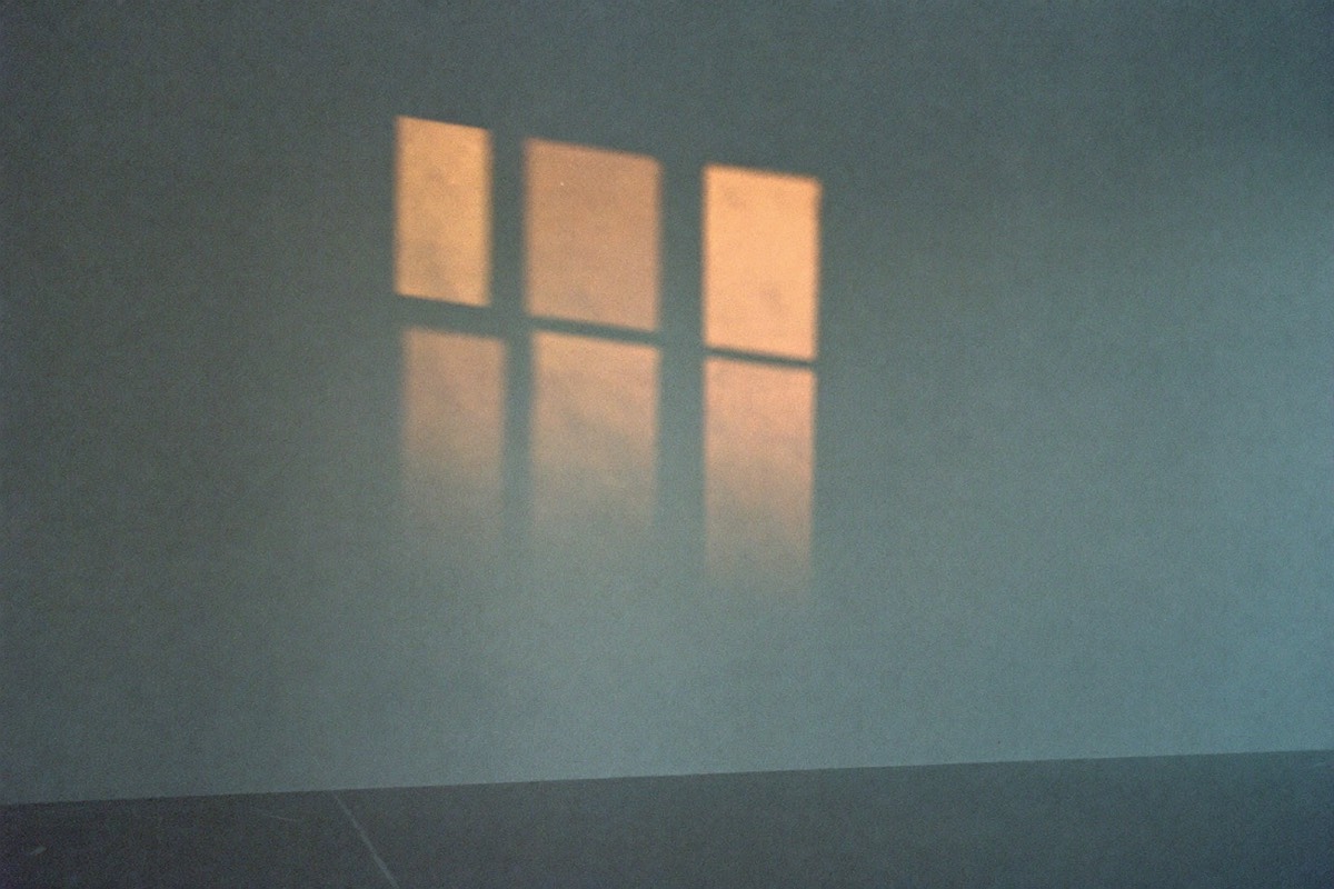 Morning light through a window casting a warm pane of sunlight across a cool, empty wall.